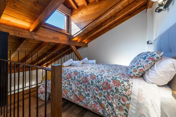 A bedroom with a sloped ceiling, a bed with floral bedding, a headboard, and a window. - Chalet 'Las Casillas' with Private Terrace, Wi-Fi, and Air Conditioning (Güejar Sierra)