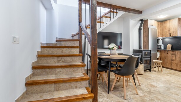 A staircase leading to a dining area with a table and chairs, a kitchen with wooden cabinets, and a large window.