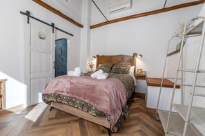 A bedroom with a wooden floor, a bed with a floral bedspread, a nightstand with a lamp, a white wardrobe, and a shower area. - Chalet 'Las Casillas' with Private Terrace, Wi-Fi, and Air Conditioning (Güejar Sierra)