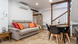 A living room with a sofa, a dining table with chairs, a staircase, and an air conditioning unit.