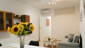 A modern living room with a sofa, a dining table with a vase of sunflowers, and a small side table. - Alcazar Historical Center V (Córdoba)