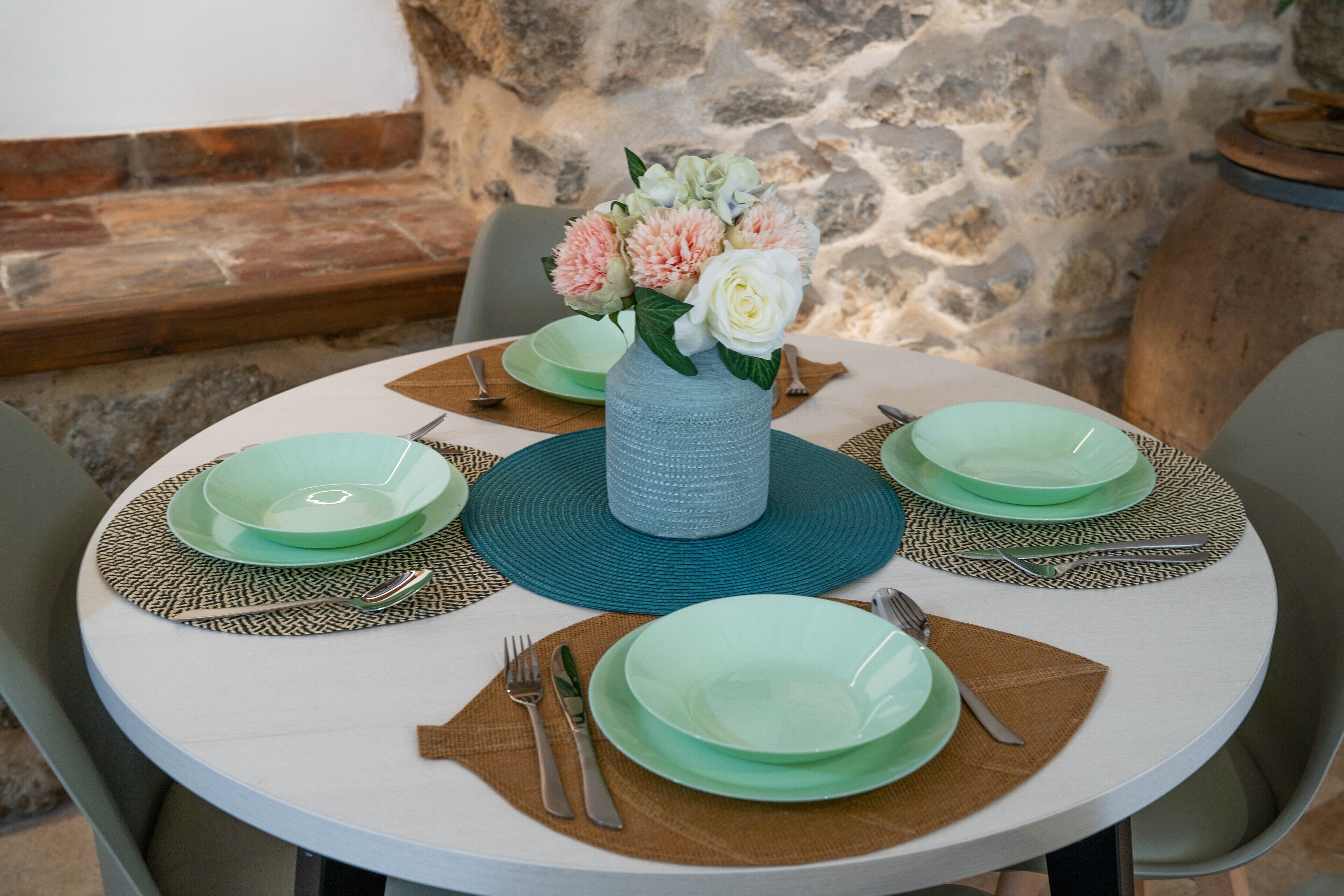 A round dining table with green plates, silverware, and a blue vase with flowers.