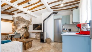 Una cocina rústica con pared de piedra, estufa empotrada, refrigerador y una cafetera roja.