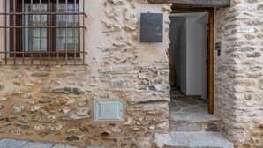 Un edificio de piedra con un vano de ventana con barrotes, una puerta con marco de madera y un timbre metálico.