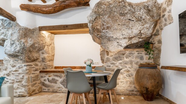 Una habitación con paredes de piedra, una mesa redonda y sillas, un banco de madera y un jarrón grande.