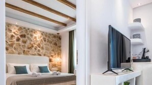 A modern hotel room with a bed, a television, a stone wall, and a white console. - Naxos Grand Hotel (Stelida)