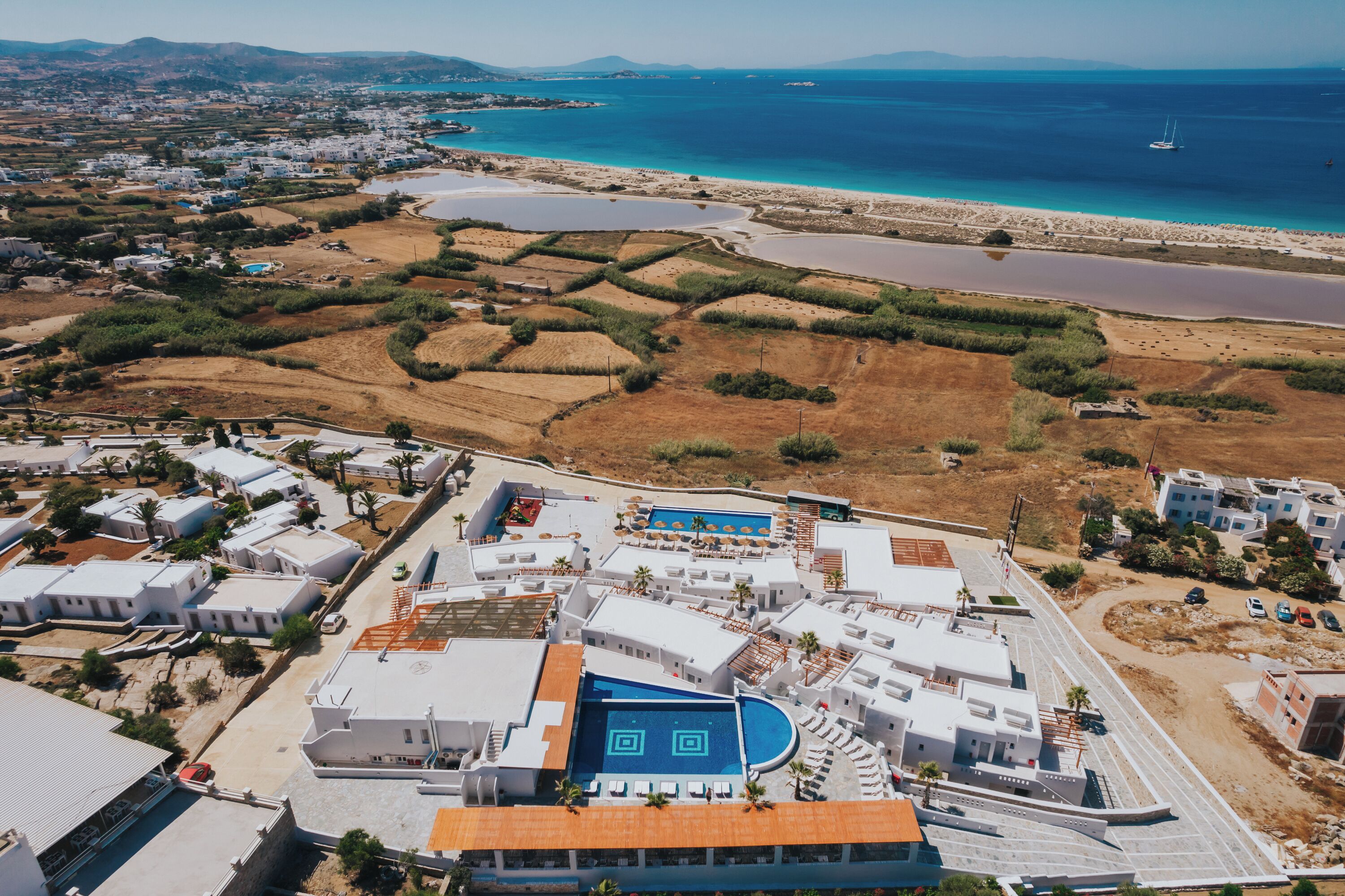 An aerial view of a coastal resort with multiple buildings, a swimming pool, and a beach.