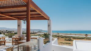 A terrace with outdoor seating, a pergola, and a view of the sea and landscape. - Naxos Grand Hotel (Stelida)