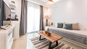 A modern living room with a sofa, a coffee table, a TV, and a dining area. - Naxos Grand Hotel (Stelida)