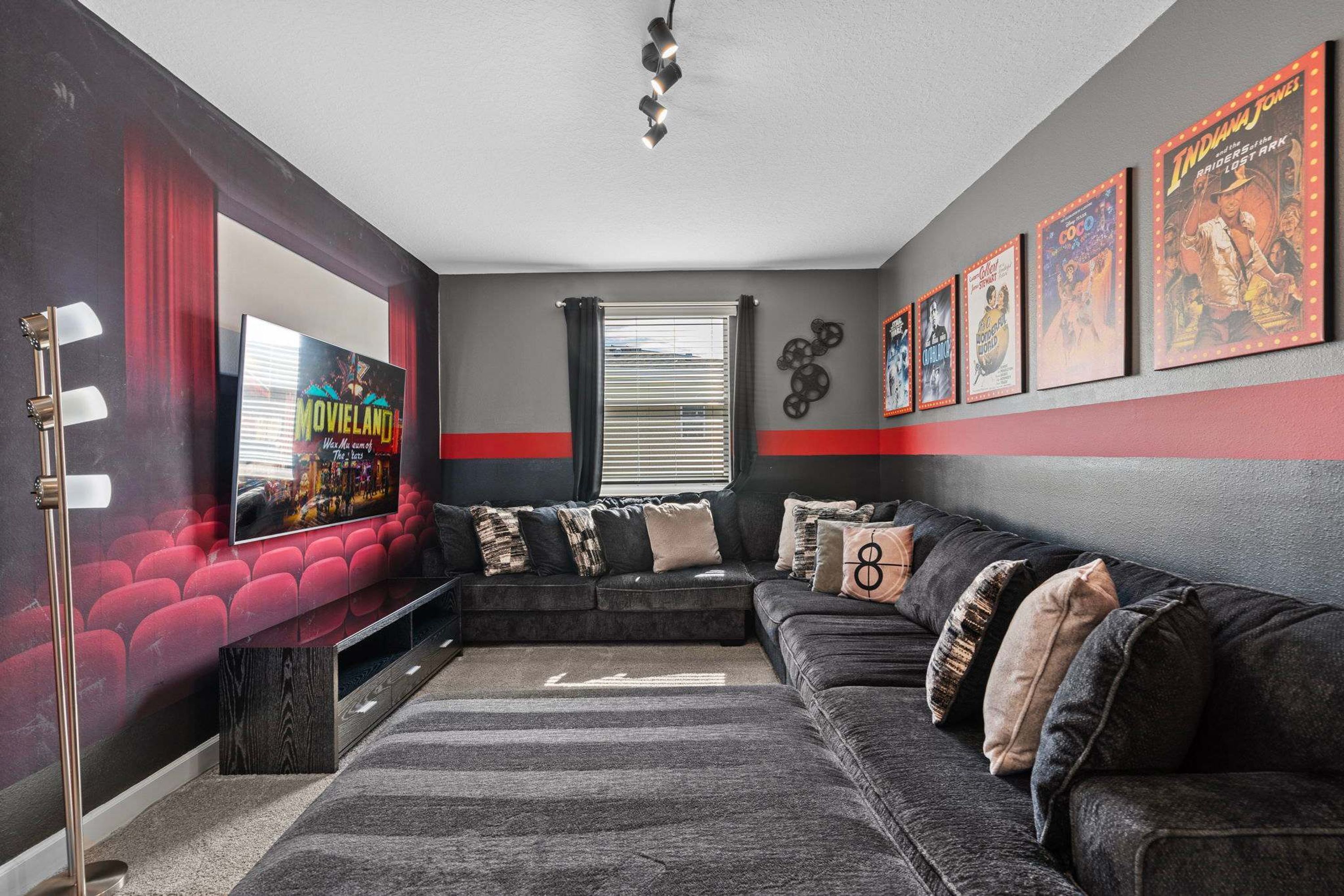 A modern living room with a sectional sofa, a large flat-screen TV, a red and grey color scheme, and movie posters on the wall.