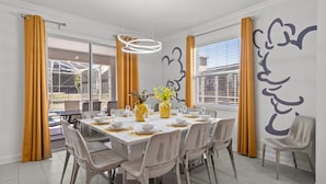 A dining area with a large table set for six, surrounded by chairs. There are two large windows with curtains, and a wall with a decorative mural. - Fully Themed 6Bed Fantasy Escape Near Disney (Four Corners)