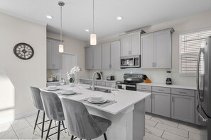 A modern kitchen with grey cabinets, a central island with seating, a microwave, and a refrigerator. - Chic 5Bed Home close to Disney parks (Four Corners)