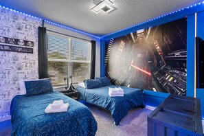 Ett sovrum med två sängar, en vägg dekorerad med Star Wars-motiv och ett stort fönster med persienner.