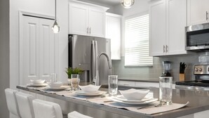 Una cucina moderna con mobili bianchi, elettrodomestici in acciaio inox e un'isola centrale con posti a sedere.