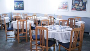 A dining area with round tables, wooden chairs, and white tablecloths. - Hotel Montañes (Suances)