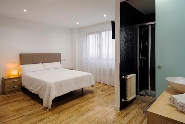 A bedroom with a bed, bedside table, and a bathroom with a shower and sink.