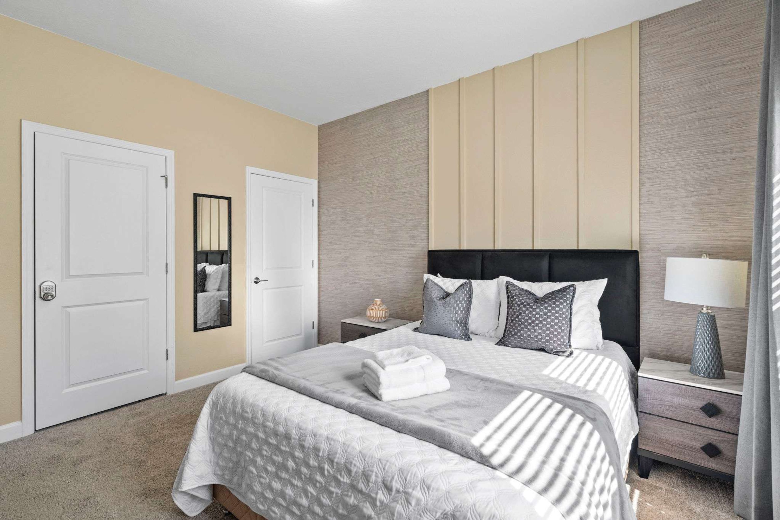 A bedroom with two beds, a nightstand with a lamp, a mirror, and a door.