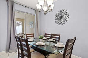 A dining area with a glass table, wooden chairs, a chandelier, and a decorative wall piece. - Spacious 4BR Townhome with Pool at Storey Lake (Kissimmee)