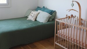 A room with a wooden floor, a green bed with pillows, a blue hanging light, and a wooden crib with a hanging toy. - T2 Panoramic sea and mountain view Beaurivage (Biarritz)