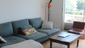 A modern living room with a sofa, a coffee table, a round ottoman, and a floor lamp. - T2 Panoramic sea and mountain view Beaurivage (Biarritz)