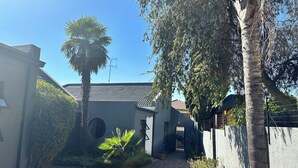 A courtyard with a paved walkway, a palm tree, and a building with a tiled roof. - Gorgeous 4-bedroom house in Meyersdal peaceful   neighborhood (Alberton)