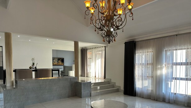 A spacious hotel lobby with a marble reception desk, a round table, a chandelier, and a staircase leading to an upper floor. - Gorgeous 4-bedroom house in Meyersdal peaceful   neighborhood (Alberton)