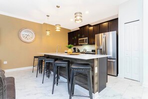 A modern kitchen with dark cabinets, stainless steel appliances, and a central island with bar stools. - Disney Area| Private Pool| Resort Waterpark 2956 (Kissimmee)