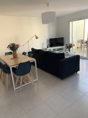 Un salon moderne comprenant un coin repas, un ensemble de canapés, un téléviseur et une table à manger avec des chaises.