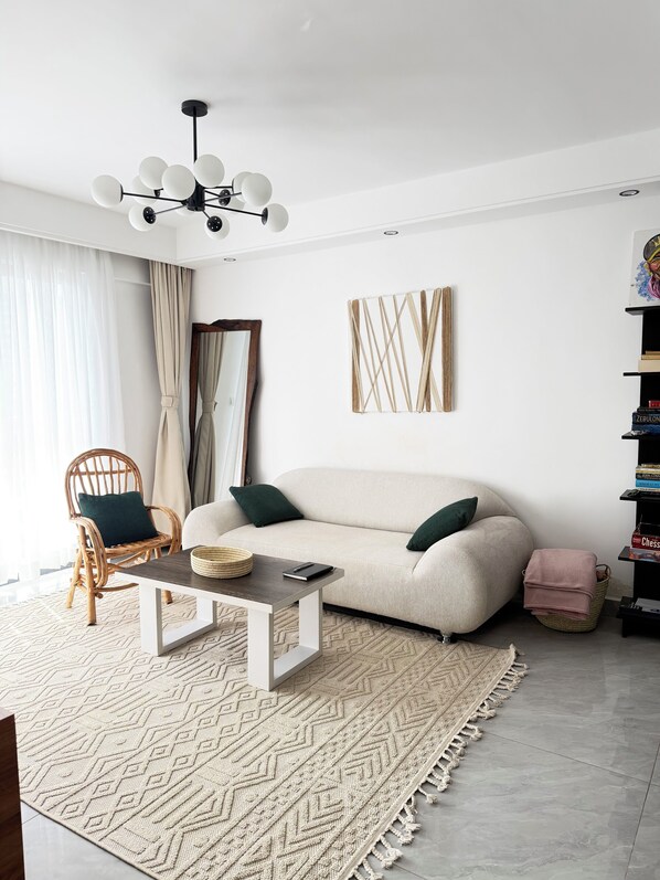 Un salon moderne avec un canapé, une table basse, un fauteuil en osier et une bibliothèque.