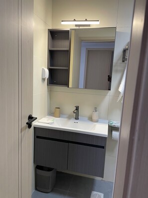 Une salle de bain moderne avec un lavabo blanc, des meubles en bois foncé, un miroir et un porte-rouleau de papier toilette.