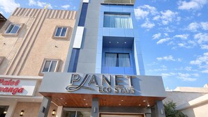 Et hotel ved navn 'Planet Eco Stays' med en moderne facade, store vinduer og et skilt for 'Patel Vanga' ved siden af.