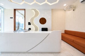 Una recepció moderna amb un disseny corbat, un detall de fusta i una zona d'espera amb una banca amb coixins.