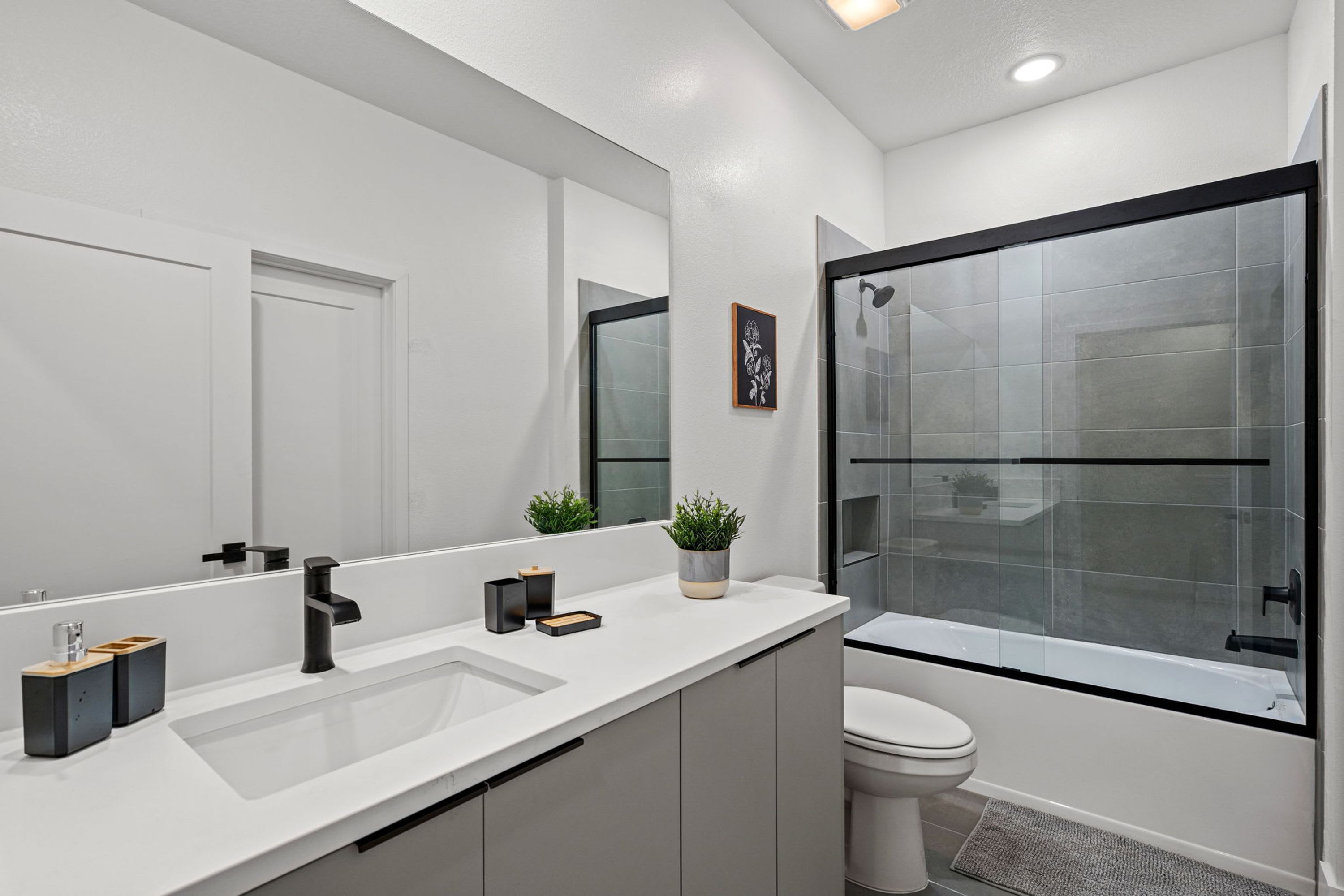A modern bathroom with a large mirror, two sinks, a toilet, and a glass-enclosed shower.