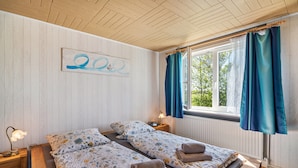 Ett rum med två sängar, ett träpanelat tak, ett fönster med gardiner, en väggklocka och ett nattduksbord med en lampa.