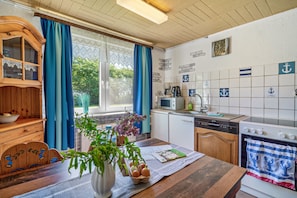 Una cocina con un armario de madera, microondas, estufa y una ventana con cortinas.