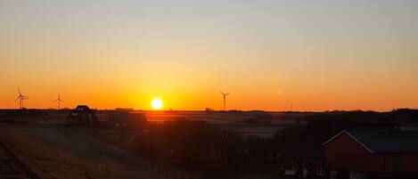 A sunset over a rural landscape with wind turbines and farm buildings.
