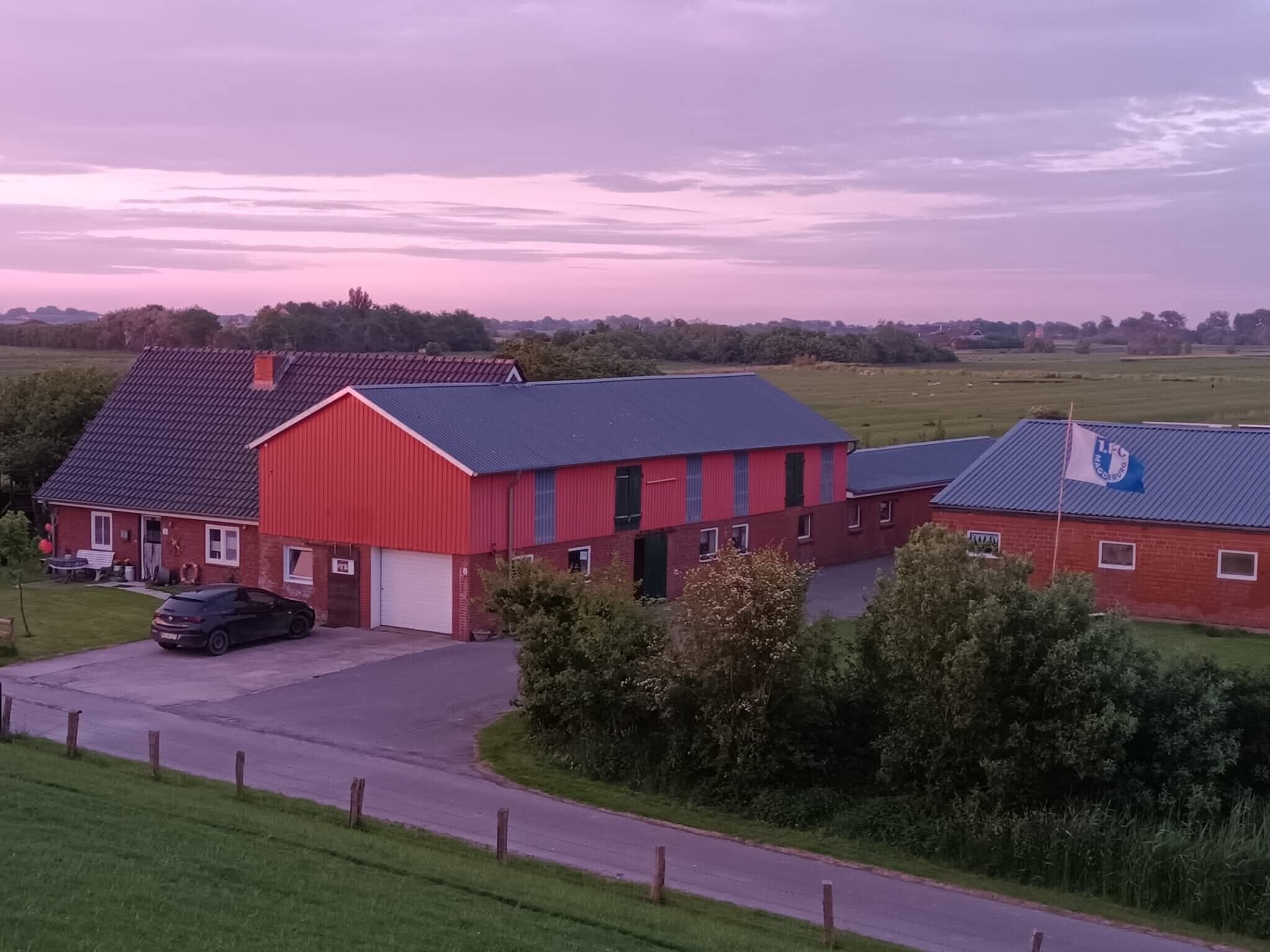 Een rode schuur met een witte garagepoort, een zwarte auto geparkeerd ervoor en een vlag op het dak.