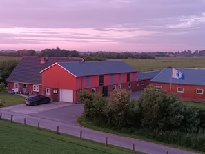 Ein rotes Bauernhaus mit einer weißen Garagentür, ein schwarzes Auto davor und eine Flagge auf dem Dach.