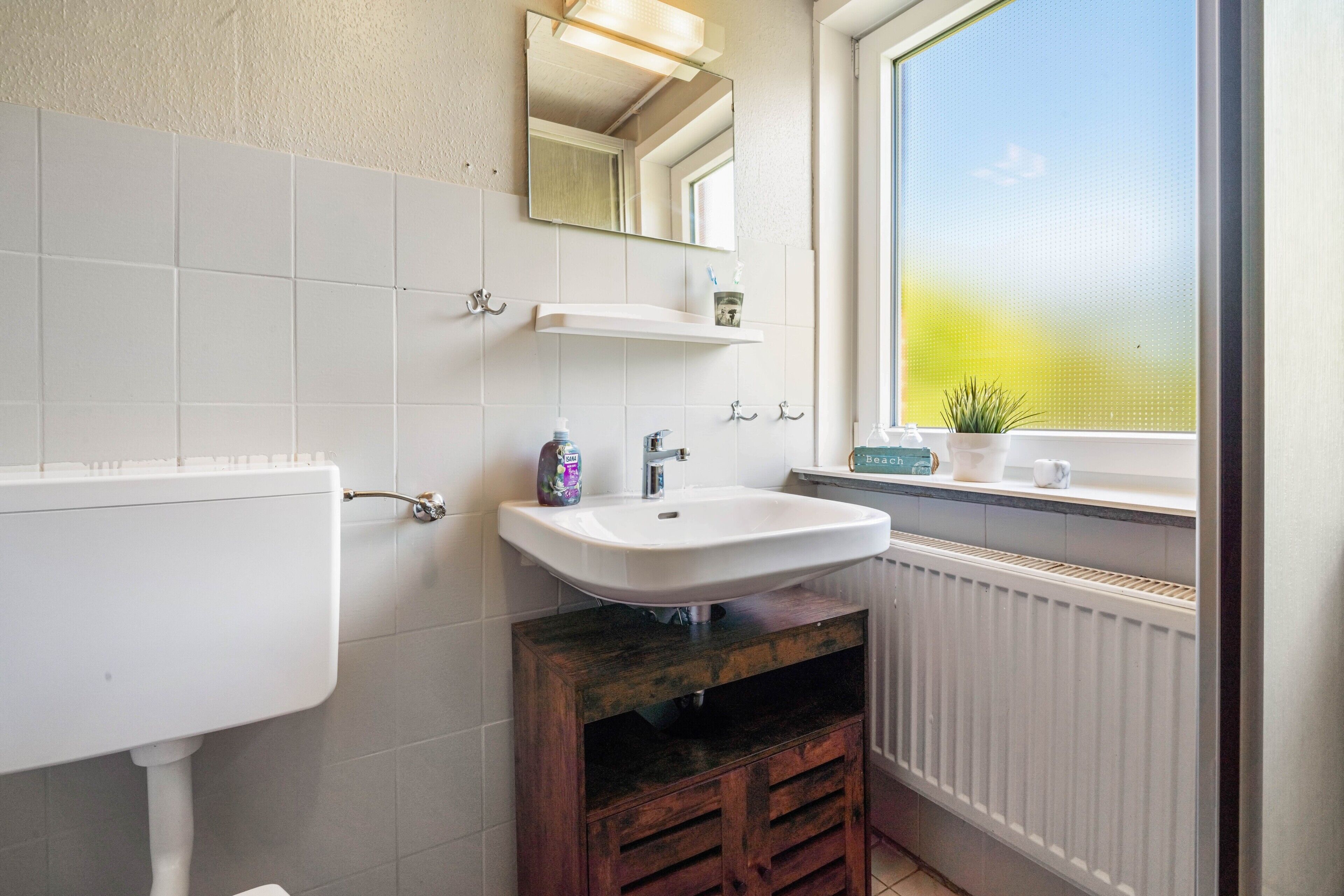 A bathroom with a white sink, mirror, and window.