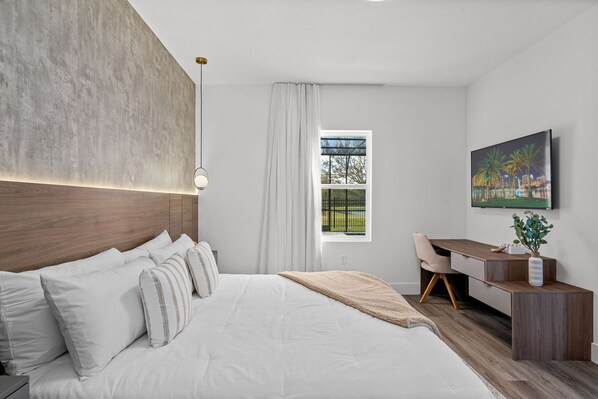 Ein modernes Schlafzimmer mit einem großen Bett, einem Schreibtisch und einem Fenster mit Blick ins Grüne.