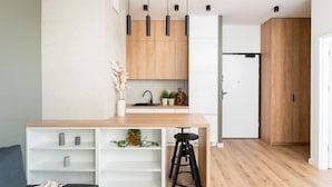 A modern kitchen with wooden cabinets, a white countertop, and a black stool. - Malila Premium Apartments Rakowicka 437 (Kraków)