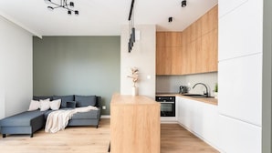 A modern living space with a grey sectional sofa, a wooden coffee table, and a kitchen area with white cabinets and wooden countertops. - Malila Premium Apartments Rakowicka 437 (Kraków)