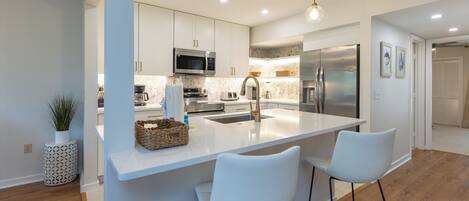 A modern kitchen with white cabinetry, stainless steel appliances, and a central island with bar stools.