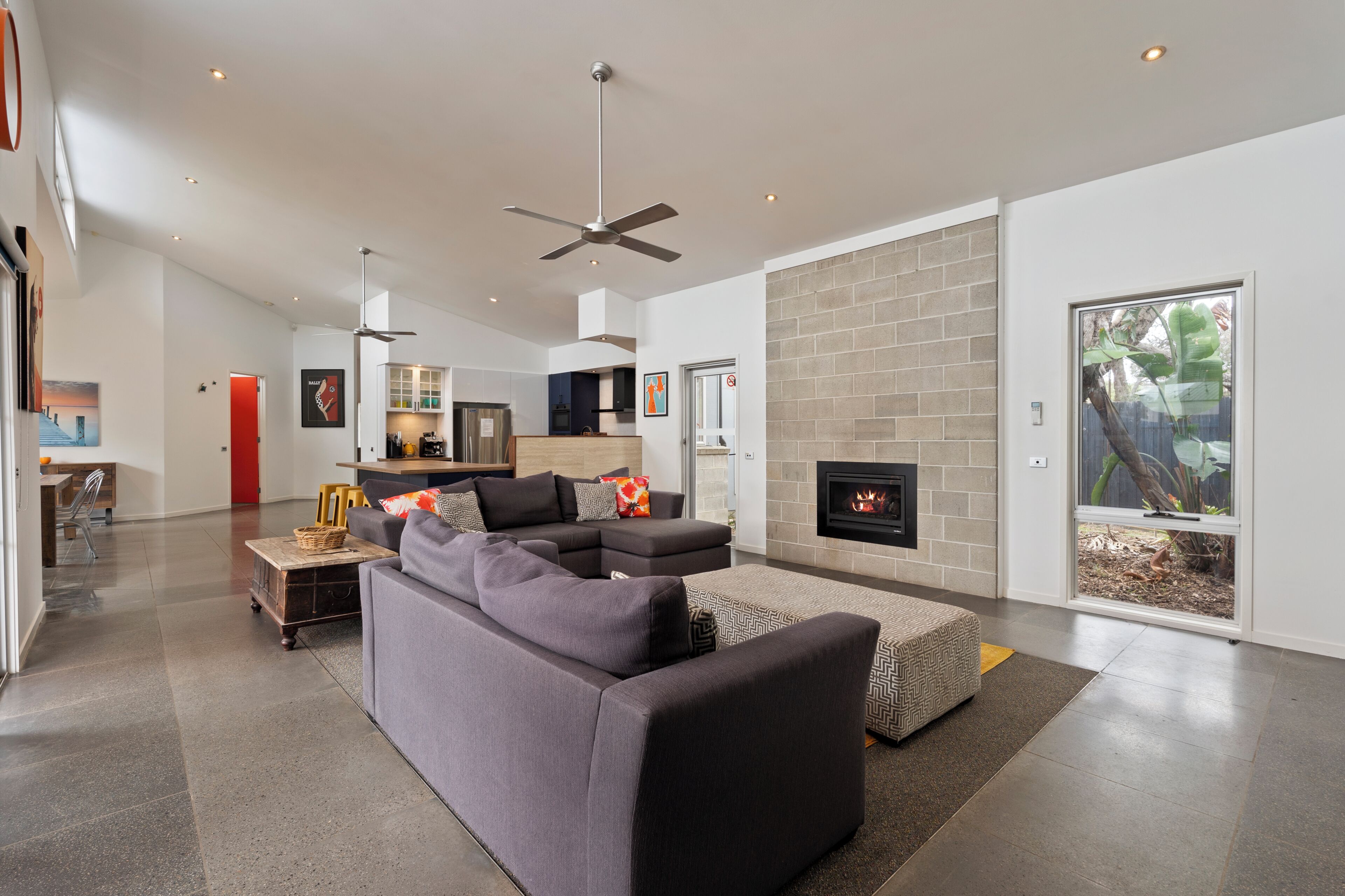 A modern living room with a sectional sofa, a fireplace, and a ceiling fan.