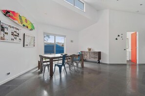 Ein geräumiges Zimmer mit Esstisch und Stühlen, einem großen Fenster und einer Wanddekoration mit Surfbrett.