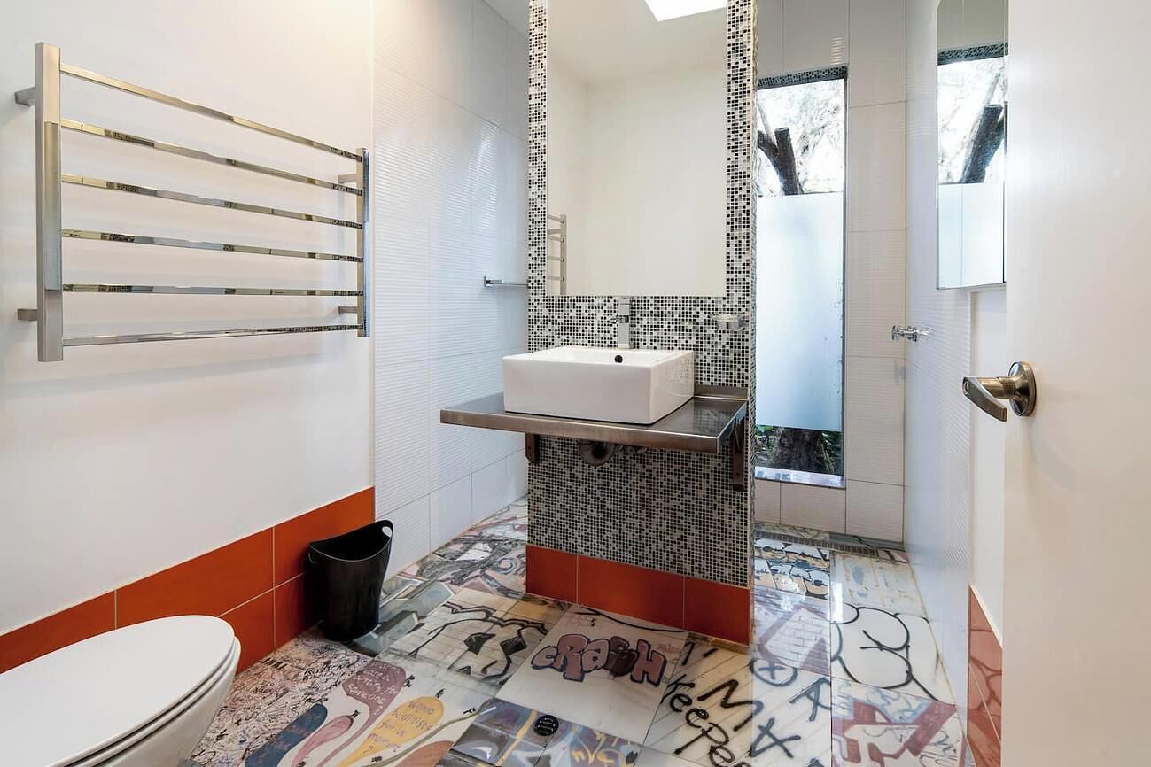 Et badeværelse med toilet, håndvask, håndklædetørrestativ og spejl.