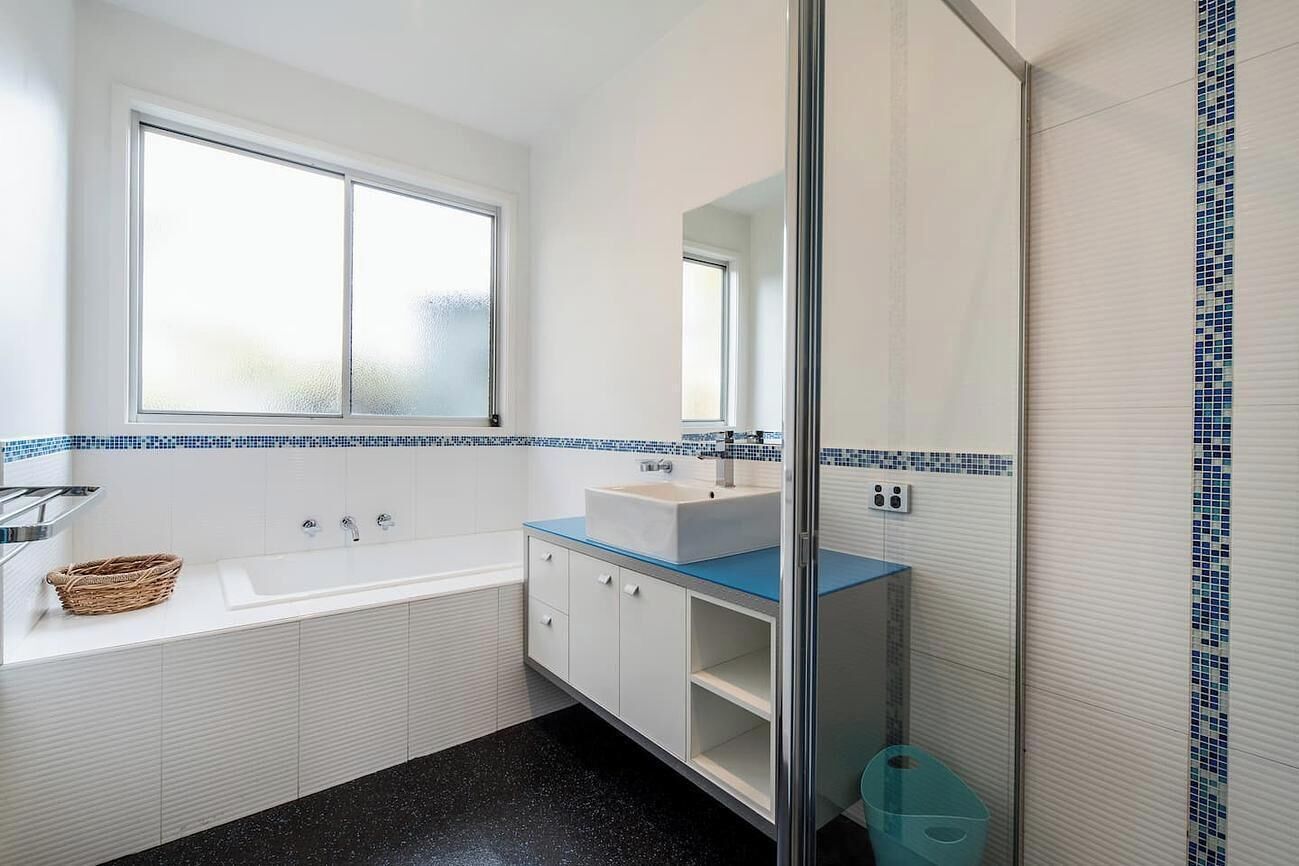 A modern bathroom with a white bathtub, a blue countertop sink, and a glass shower enclosure.
