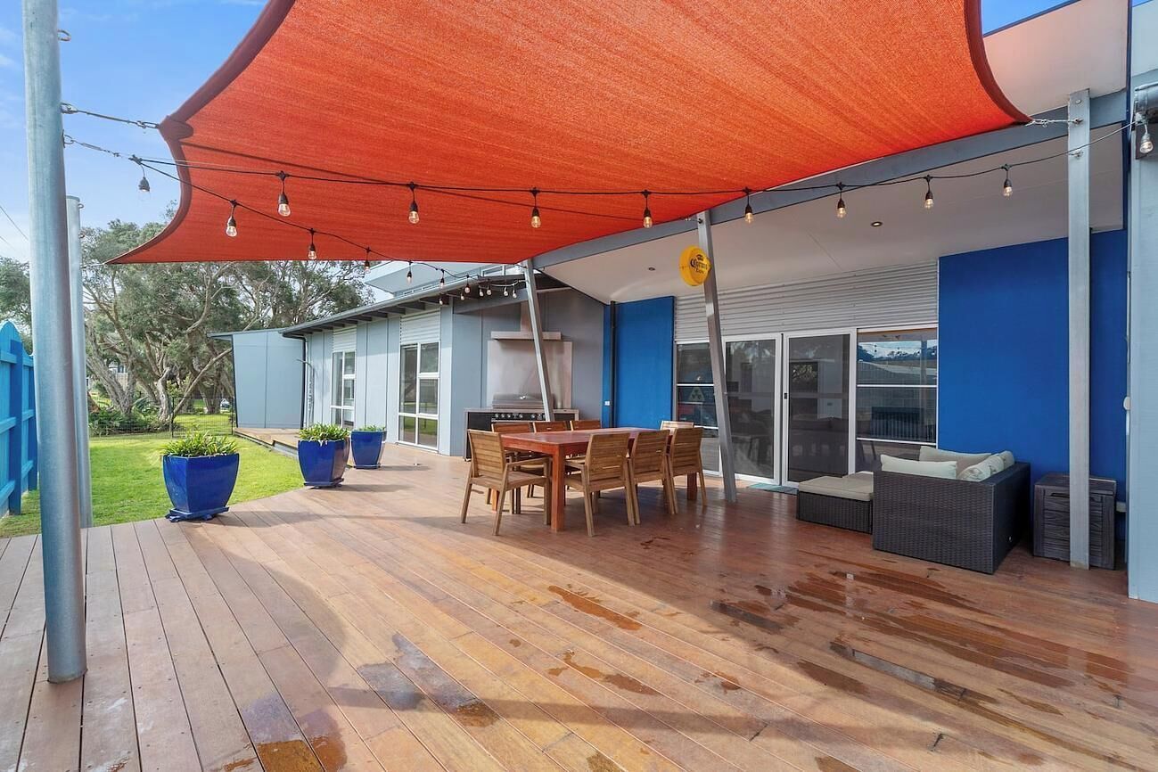 Een terras buiten met een houten terras, een tafel met stoelen, een barbecue en een overdekte zithoek.