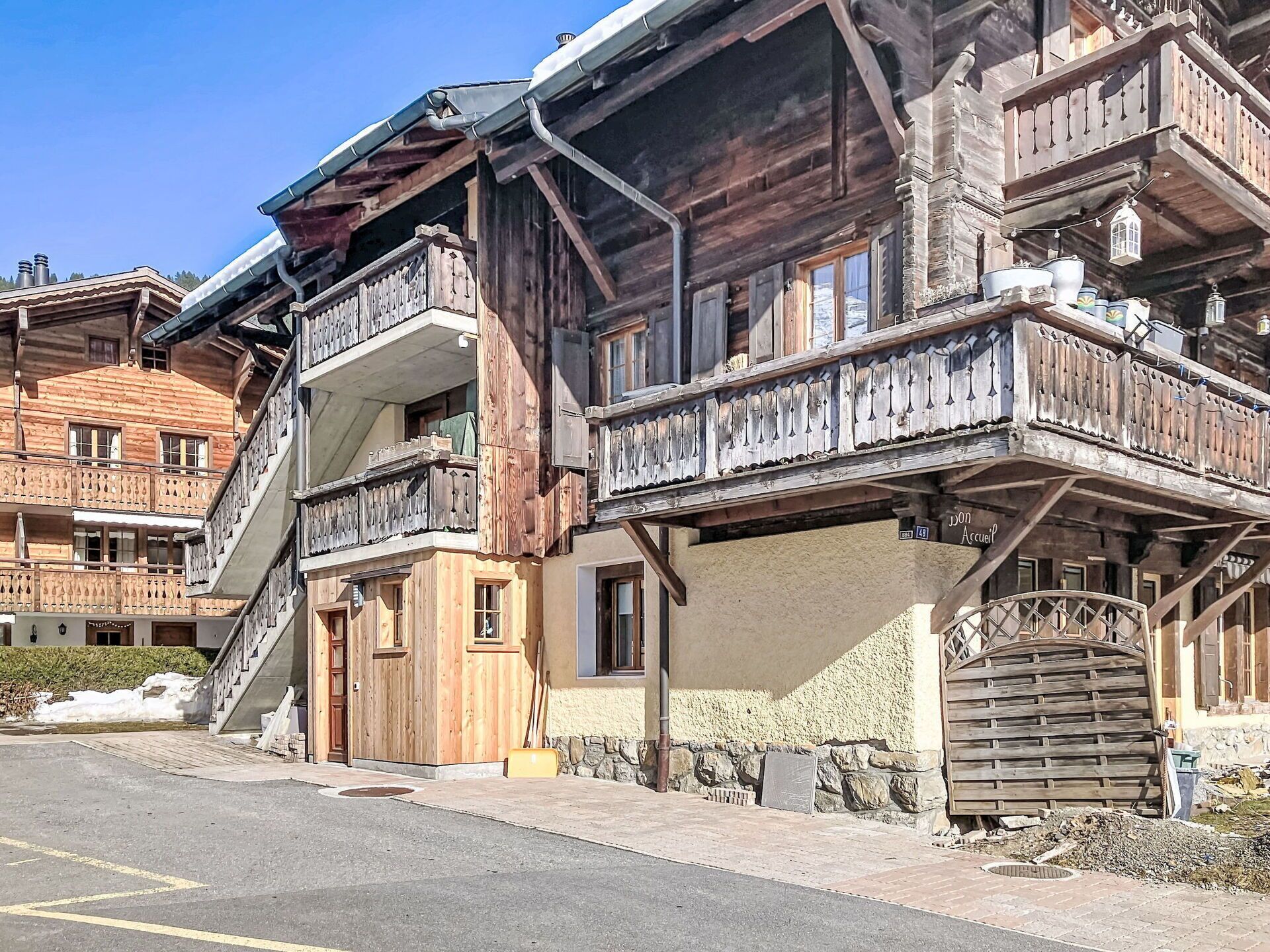 Ein mehrstöckiges Holzhaus mit Balkonen, einer Steinmauer und einer gut sichtbaren Eingangstür.