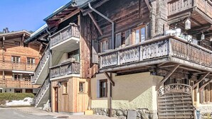 Un edificio de madera de varios pisos con balcones, un muro de piedra y una entrada visible.